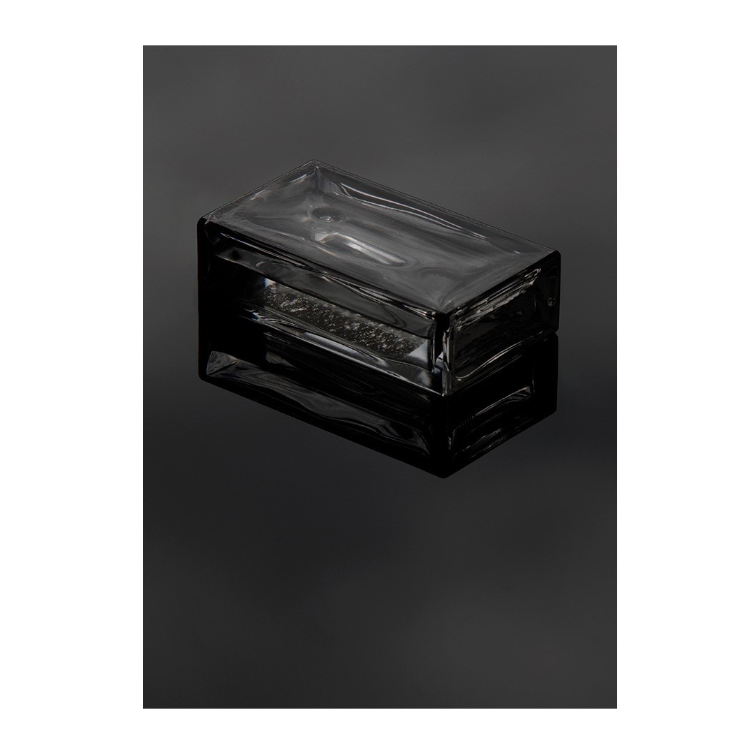 Rectangular clear glass brick resting on a glossy black surface with strong reflection, minimalist, product shot.
