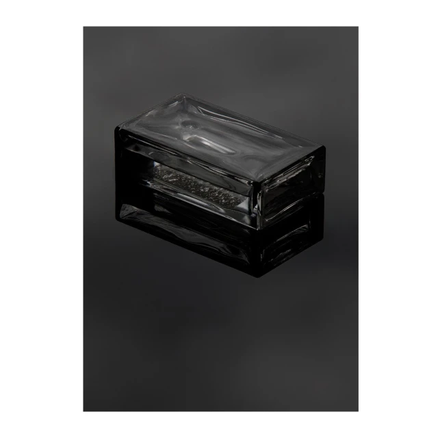 Rectangular clear glass brick resting on a glossy black surface with strong reflection, minimalist, product shot.