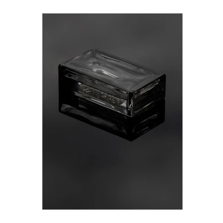Rectangular clear glass brick resting on a glossy black surface with strong reflection, minimalist, product shot.