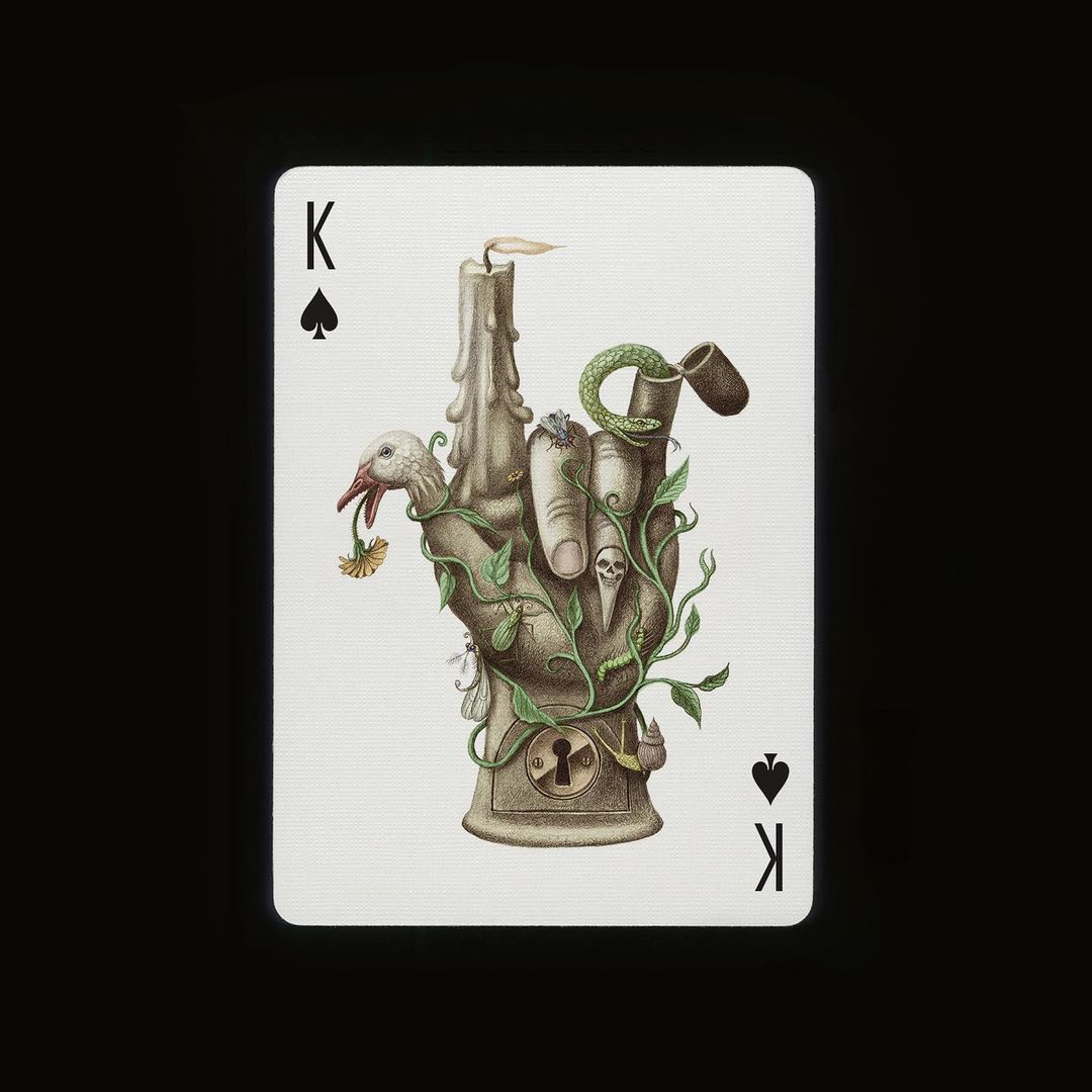 Intricate art playing card featuring a stone-like hand with a candle on top, adorned with foliage, a snake, a bird, and skulls.
