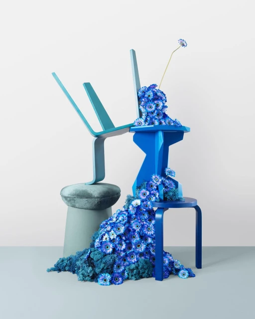 Blue and turquoise chairs adorned with blue daisy flowers against a white backdrop, creating a vibrant and artistic composition.