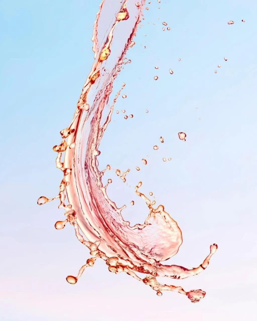 A splash of translucent, light pink liquid against a gradient light blue to pink background, creating a dynamic, abstract composition.