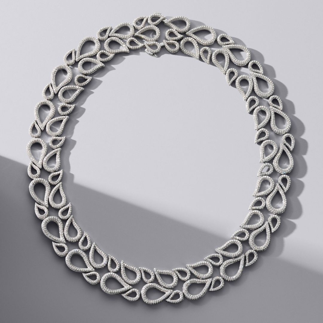 Overhead shot of a sparkling diamond necklace featuring teardrop-shaped gems against a grey background with a soft shadow.