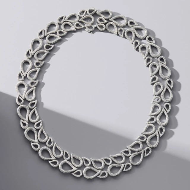 Overhead shot of a sparkling diamond necklace featuring teardrop-shaped gems against a grey background with a soft shadow.