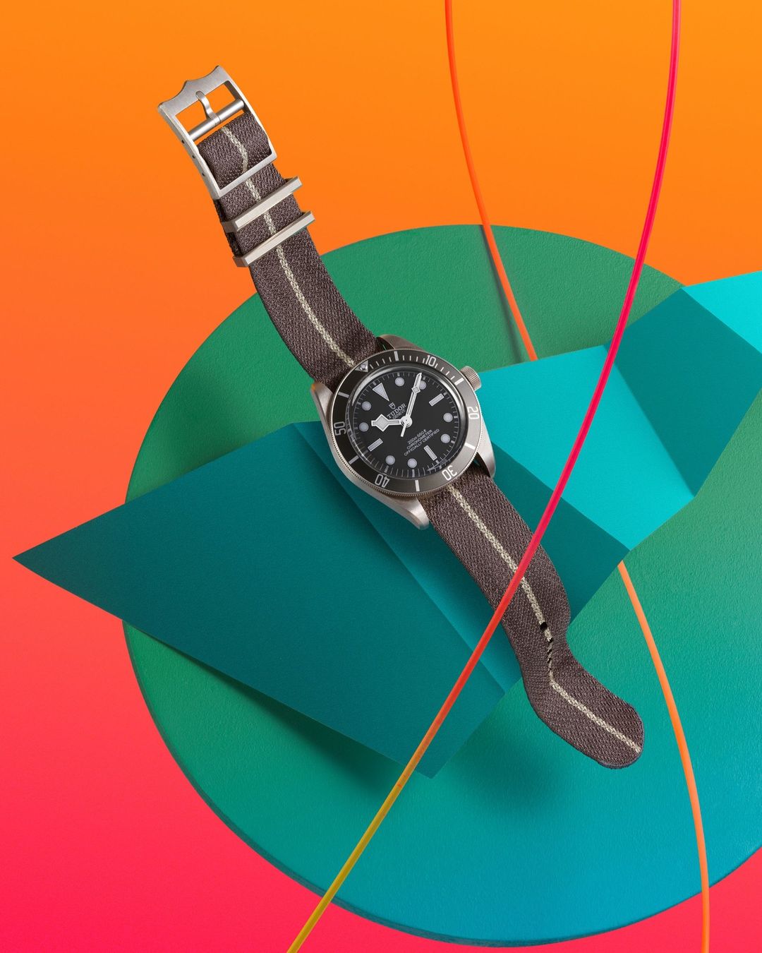 Wristwatch with a gray and white striped band displayed on teal geometric shapes, set against a vibrant gradient background.