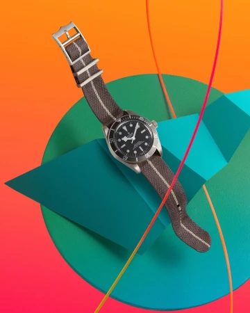 Wristwatch with brown fabric strap resting on abstract geometric teal and orange studio set with curved lines
