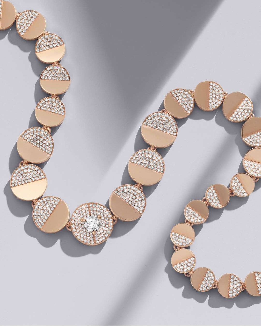 Rose gold diamond necklace arranged in a curved line on a clean grey background with soft shadows