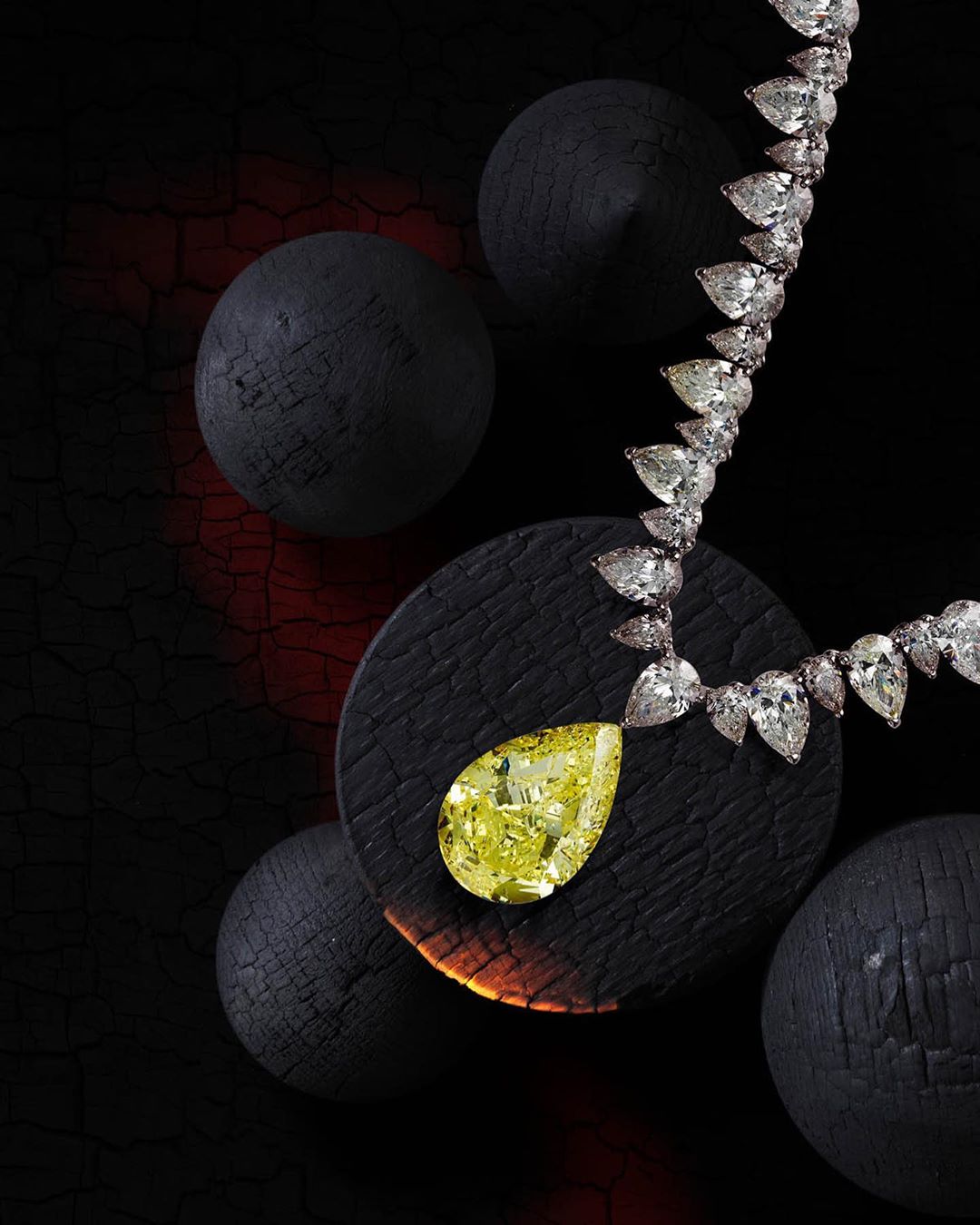 Necklace featuring pear-shaped yellow diamond pendant on dark wood against a dark background with black spherical wooden objects.