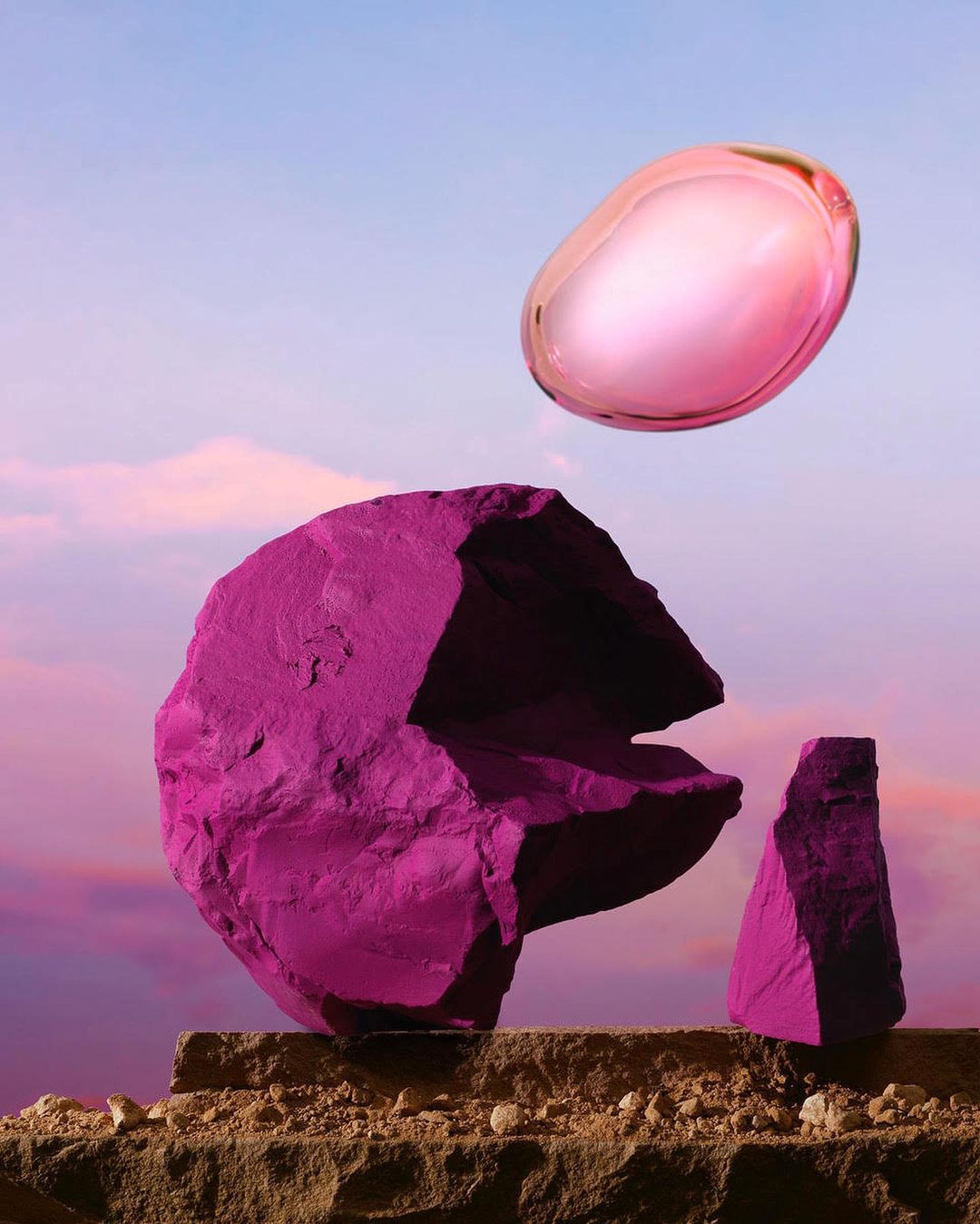 Abstract product shot: Pink, magenta-painted rocks are stacked on a stone ledge with a floating, translucent pink sphere overhead against a dusk sky.