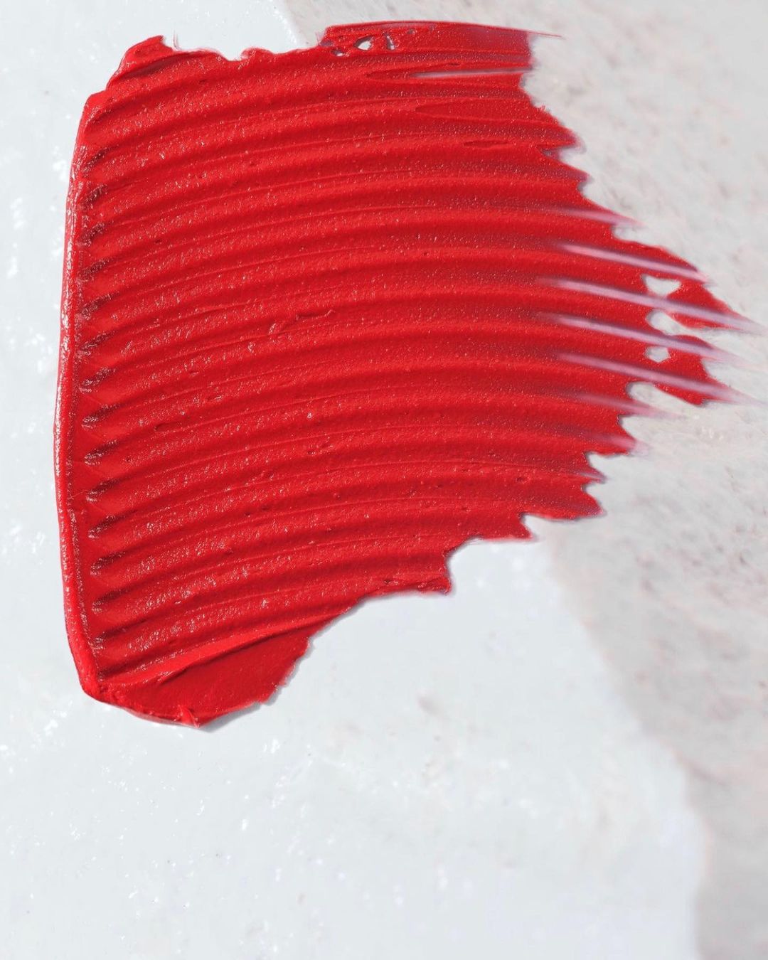 Close-up of a smear of bright red lipstick on a white surface, showcasing the texture and color of the cosmetic product.