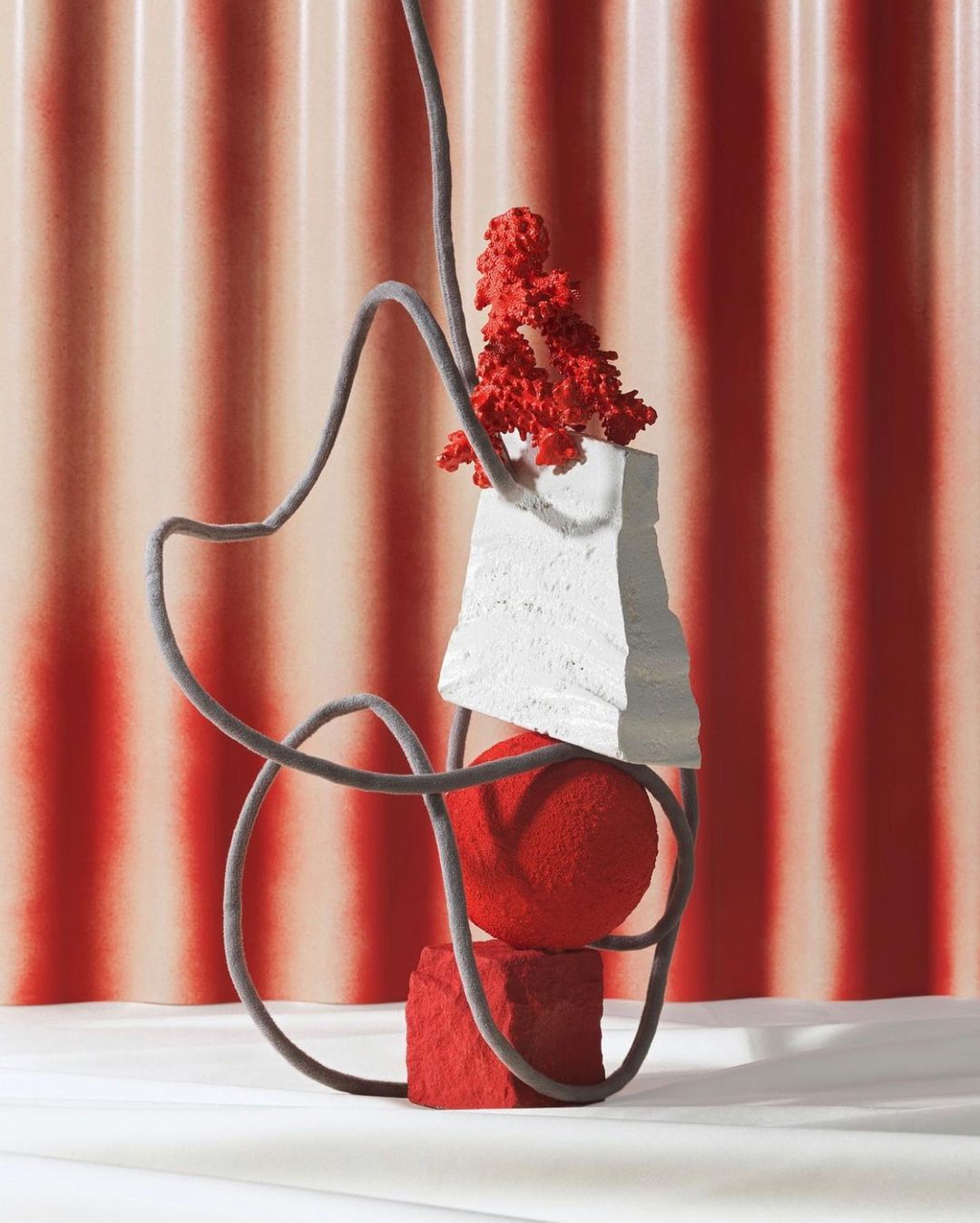 Abstract still life composition featuring red and white textured geometric shapes, a flexible gray tube, and a striped pink backdrop.