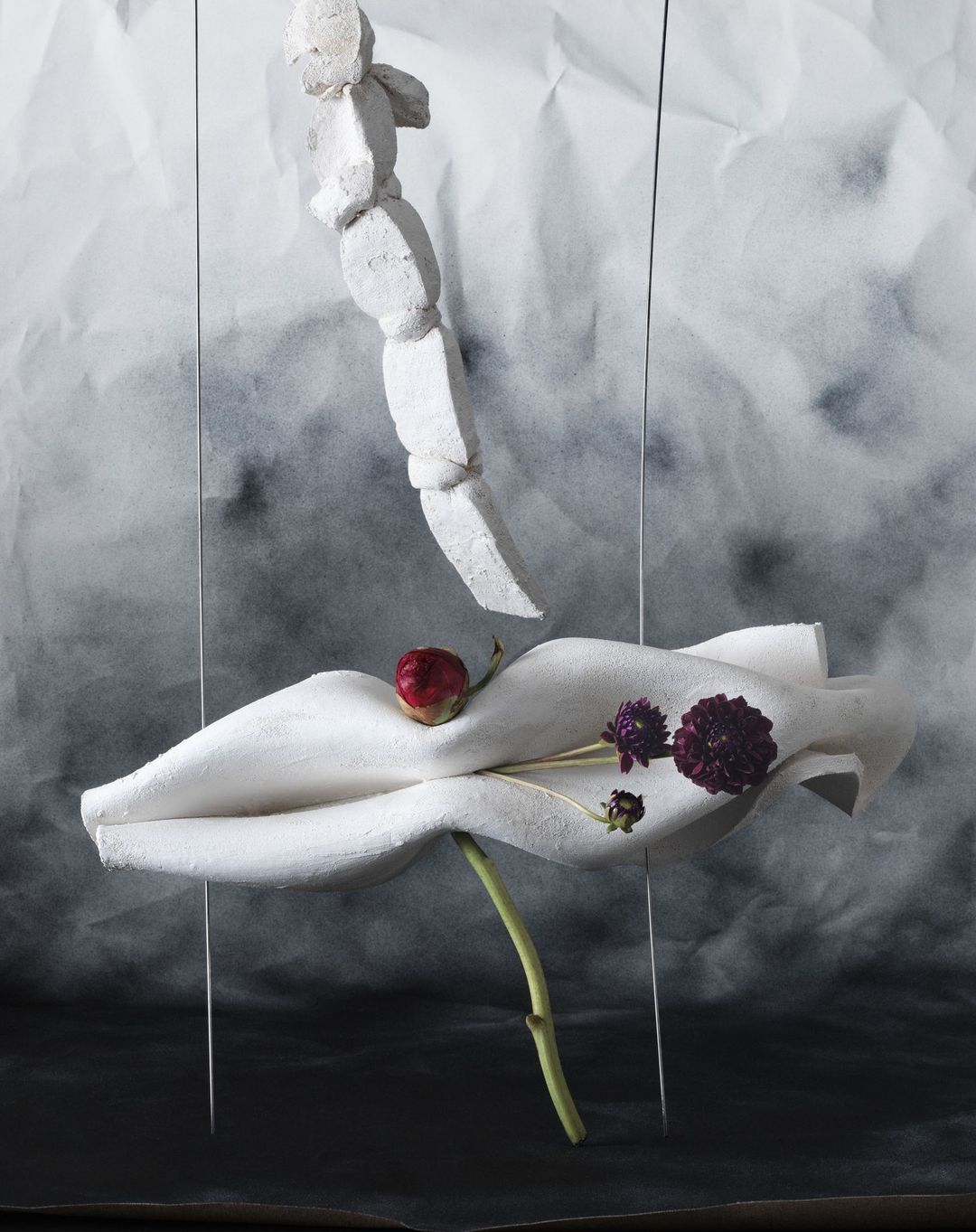 Artistic still life with a plaster figure, flowers, and textured backdrop creating a surreal and visually intriguing composition.