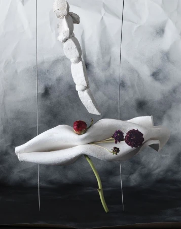 Artistic still life with a plaster figure, flowers, and textured backdrop creating a surreal and visually intriguing composition.