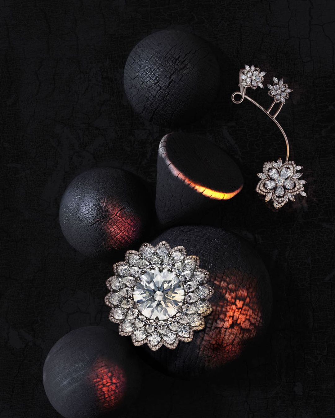 Still life showcasing fine jewelry, including a floral brooch and a delicate earring, displayed against dark textured spheres.