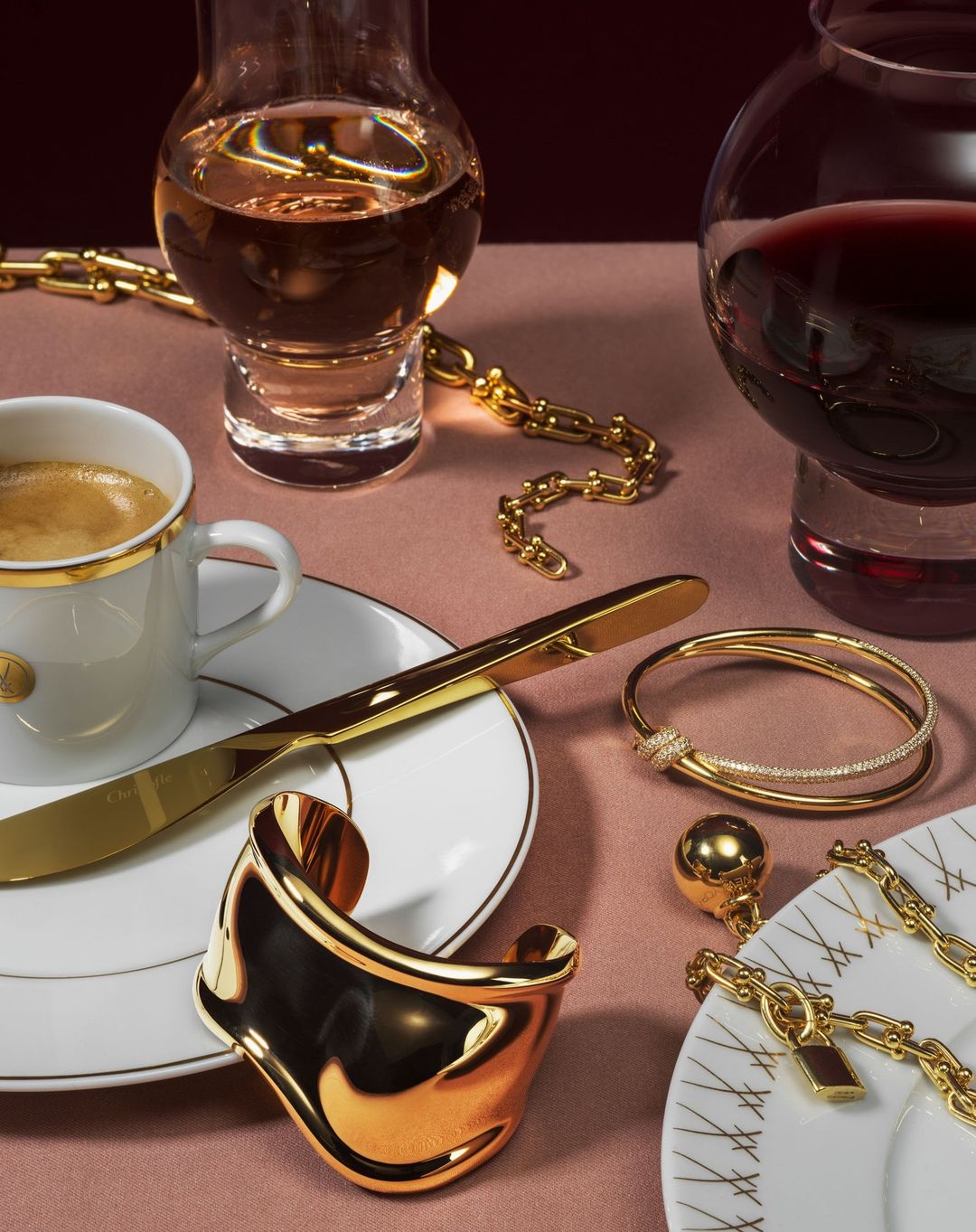 Still life shot with gold jewelry arranged among glassware and tableware, creating a luxurious and artistic composition.