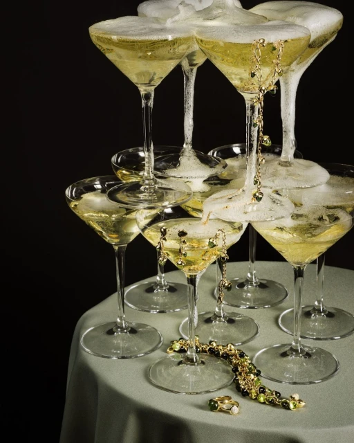 Tower of champagne glasses filled with sparkling wine and foam, accessorized with a gold ring and jewelry on a table.