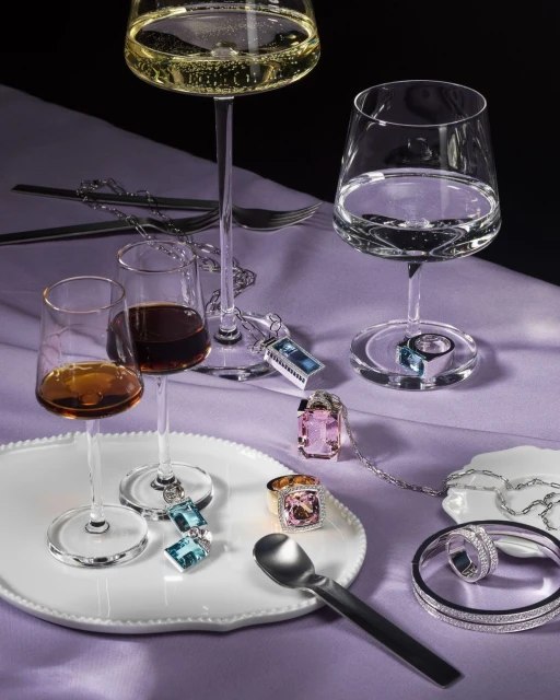 Close-up of highball glasses with clear and amber liquors alongside assorted silver jewelry on a white tray and lavender tablecloth.