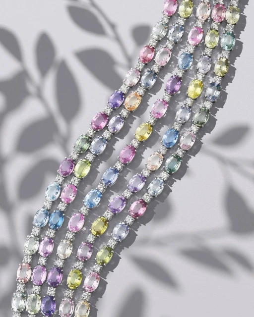 Overhead studio shot displays five delicate gemstone bracelets with colorful pastel gems and diamond accents on a pale gray surface.