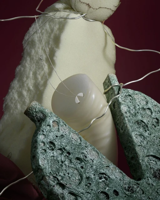 Abstract still life featuring textured stone, an off-white vase, soft white foam, and wire set against a dark red backdrop.