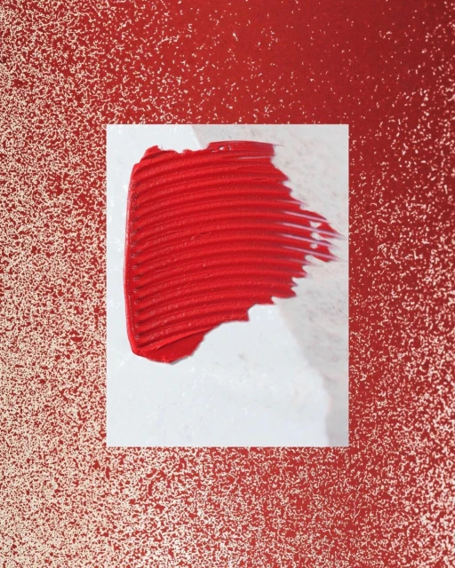 Abstract close-up of a smear of red lip gloss on a white surface against a speckled red backdrop. Cosmetics beauty background.