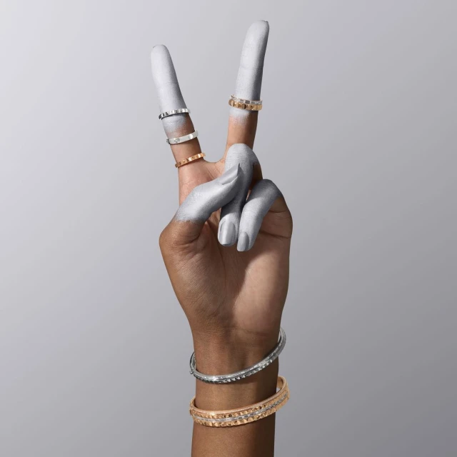 Hand painted silver making a peace sign with jewelry including rings and bracelets against a grey backdrop in a studio.
