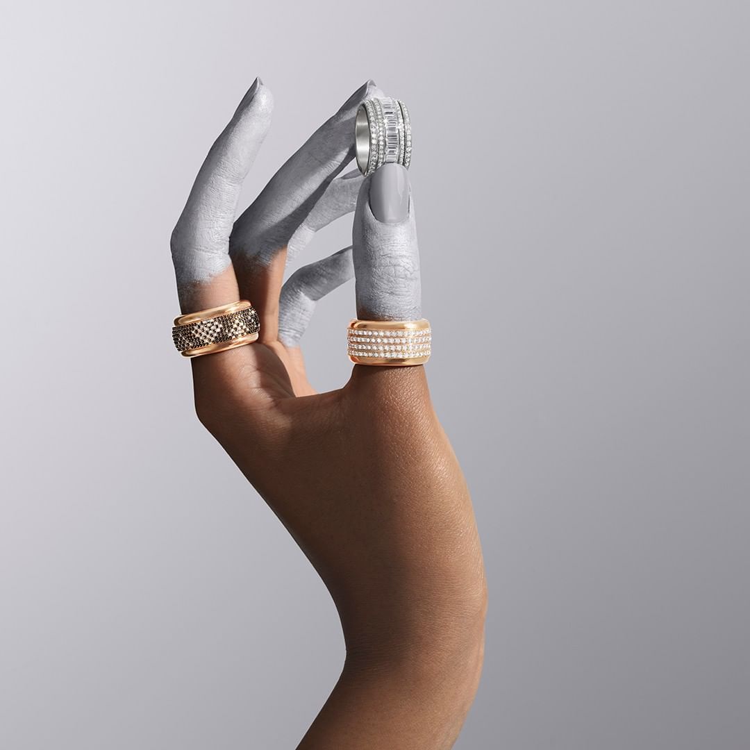 Hand painted in grey holding rings. Close-up of a hand wearing a gold ring, silver ring, and diamond ring against a grey background.