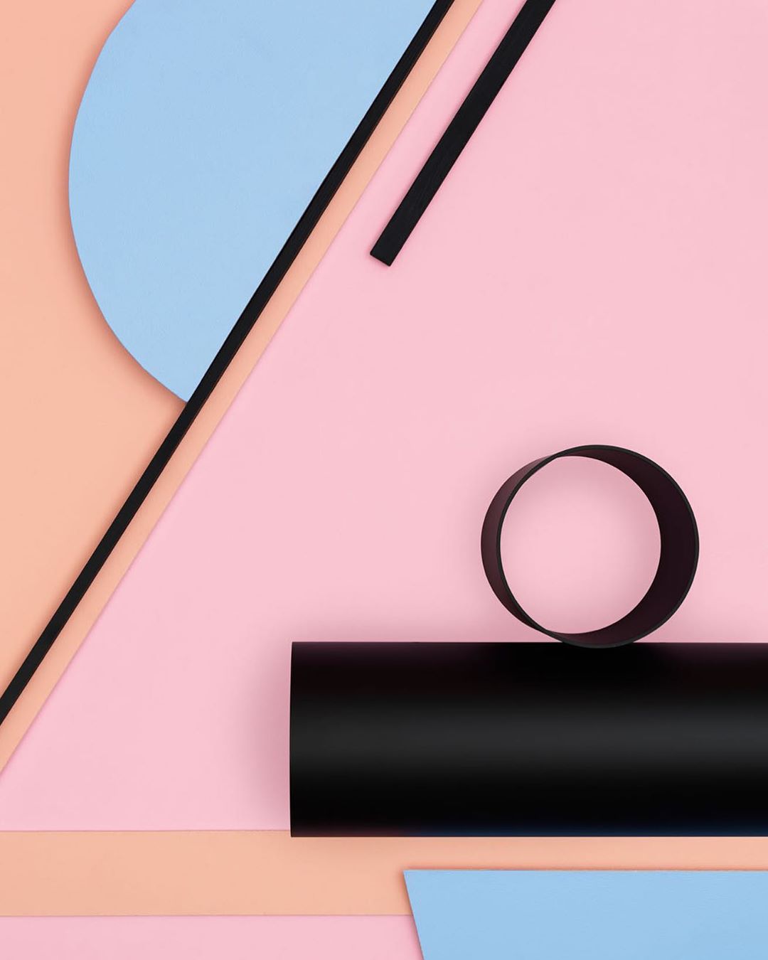 Abstract geometric composition of intersecting pastel paper shapes in pink, blue, and peach, with black paper bars and cylinder.