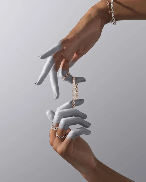 Two silver-painted hands display a ring and bracelet against a light gray background, showcasing fashion jewellery in a modern, minimalist style.