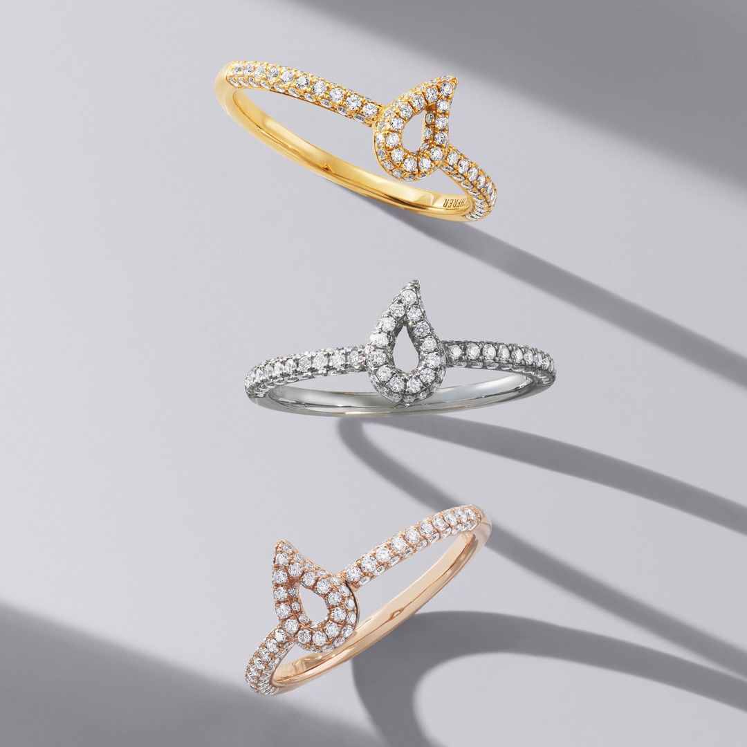 Three rings with diamond accents are displayed on a gray surface with soft shadows, showcasing jewelry for fashion and beauty.