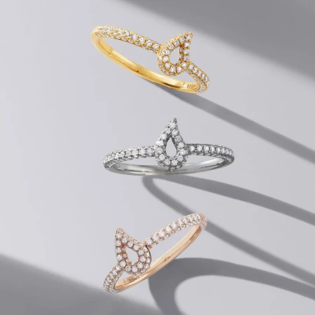 Three rings with diamond accents are displayed on a gray surface with soft shadows, showcasing jewelry for fashion and beauty.