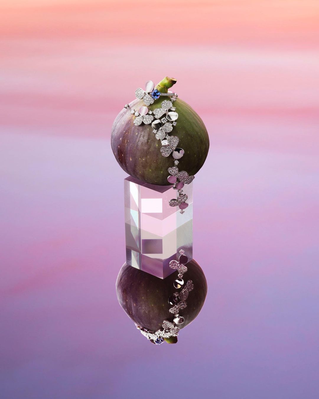 Close-up of a fig adorned with jewelry on a reflective cube. The composition has an ethereal quality, set against a soft gradient backdrop.