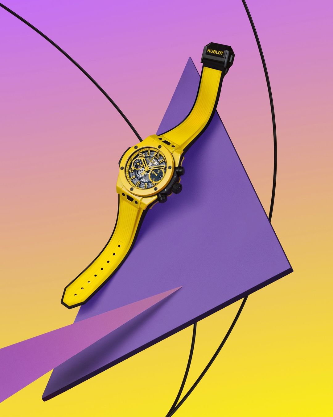 Luxury yellow wristwatch floating on purple and yellow background with geometric shapes and modern design in an indoor setting.