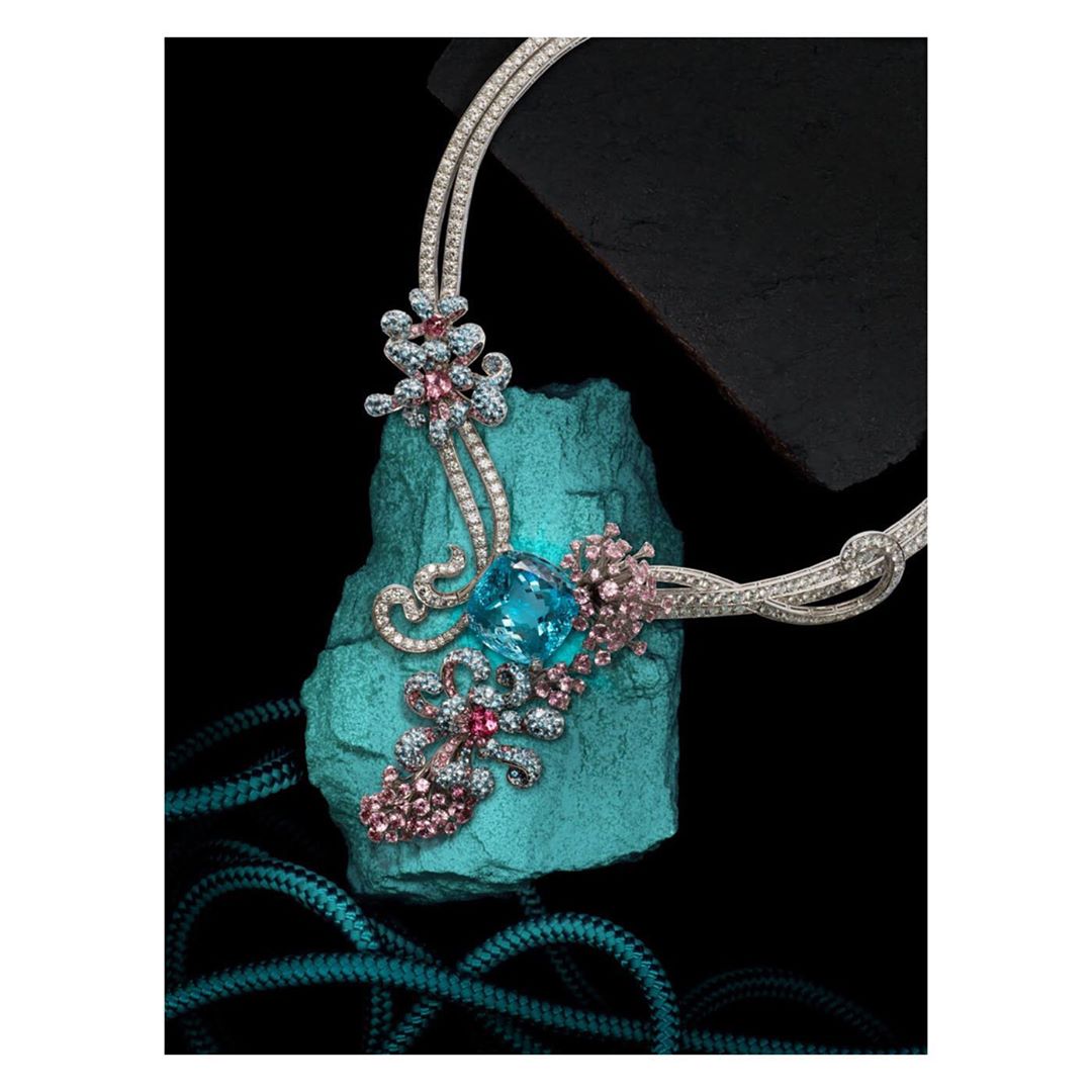 Elegant silver necklace with floral design and large aquamarine gemstone centerpiece, displayed on an aqua-colored rock against black background.