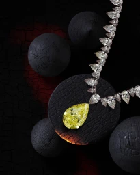 Close-up of a diamond necklace featuring a large pear-cut yellow diamond resting on dark textured spheres against a black background.