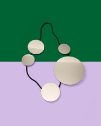 Abstract metallic circular necklace sculpture with a thin black cord against a split green and lilac background.