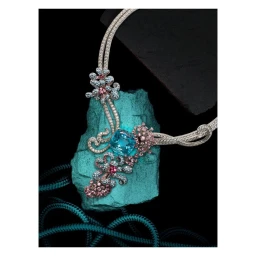 An ornate silver diamond necklace with blue and pink gemstones resting on a textured turquoise mineral stone against a black background.