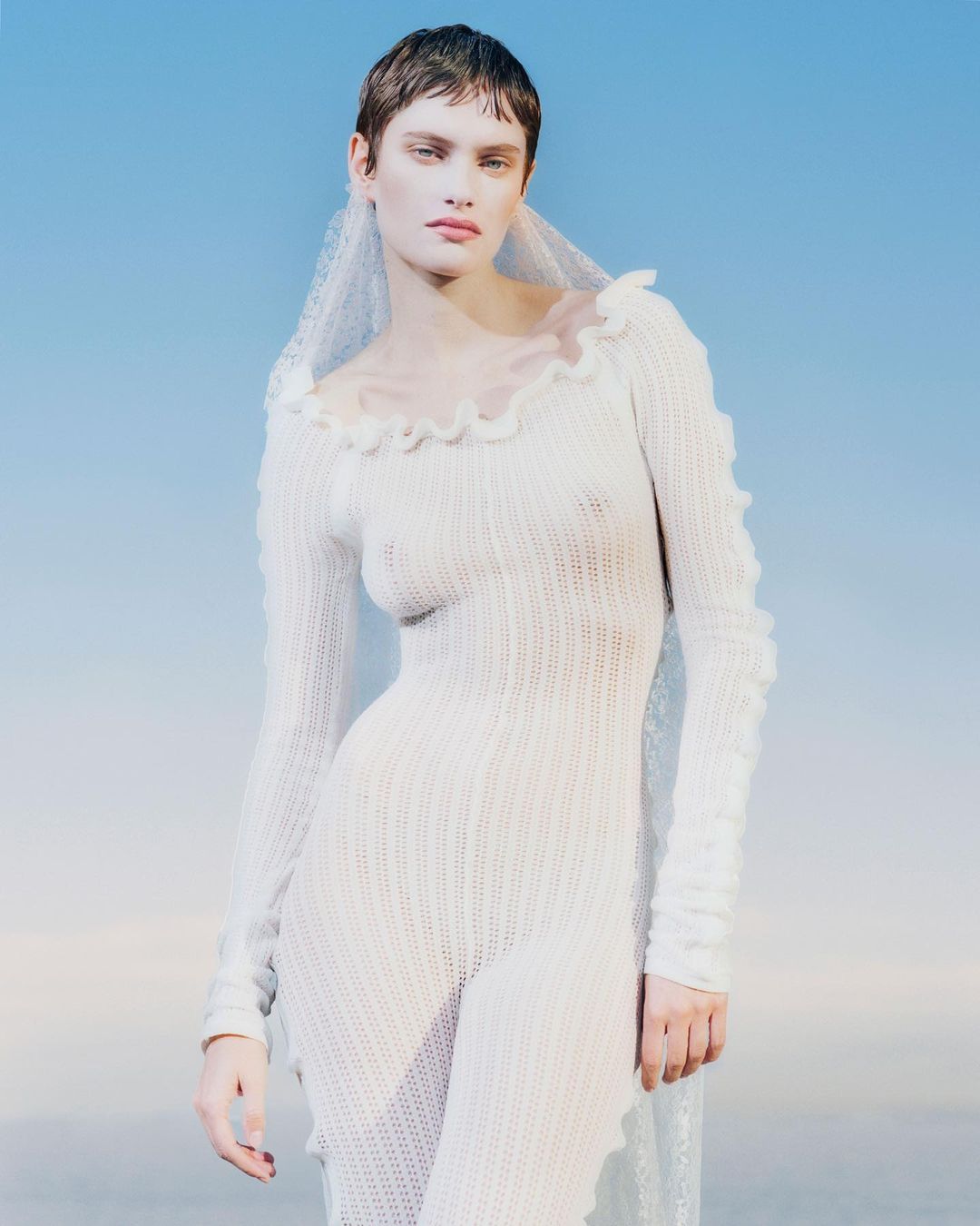 Woman poses wearing a knit jumpsuit and veil against a blue gradient background. Close-up portrait. Fashion advertisement.