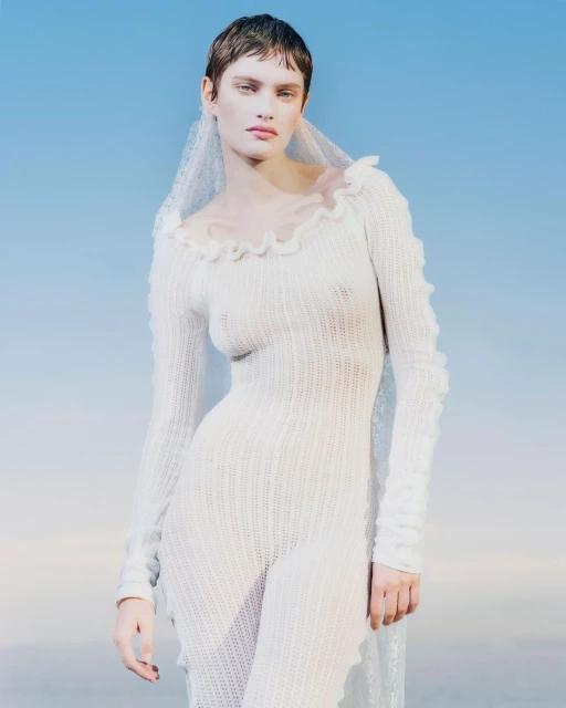 Woman poses wearing a knit jumpsuit and veil against a blue gradient background. Close-up portrait. Fashion advertisement.