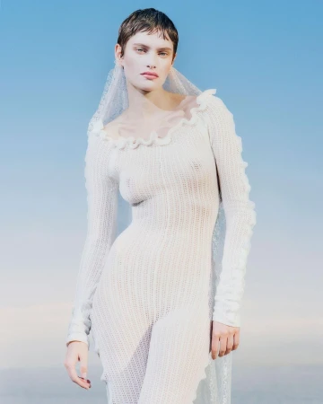 Woman poses wearing a knit jumpsuit and veil against a blue gradient background. Close-up portrait. Fashion advertisement.