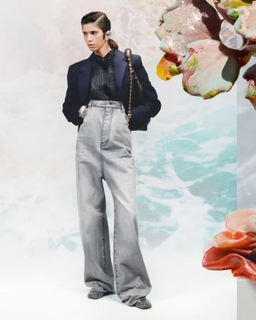Model in high-waisted grey denim jeans and navy blazer standing against a pale abstract background by Arnaud Lajeunie