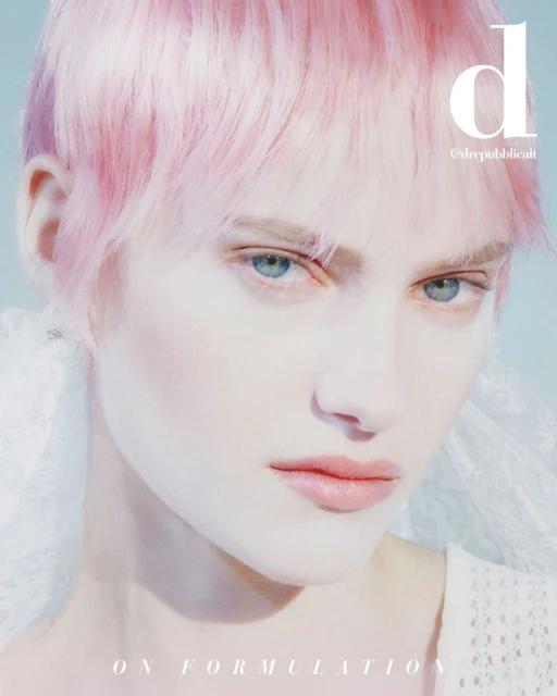 Close-up portrait of a fair-skinned adult female model with pink hair and light eyes in a studio setting with diffused lighting.