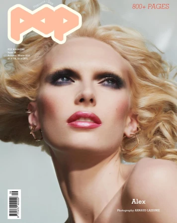 Close-up portrait of a blonde woman with dramatic smokey eye makeup and glossy pink lips against a plain background.