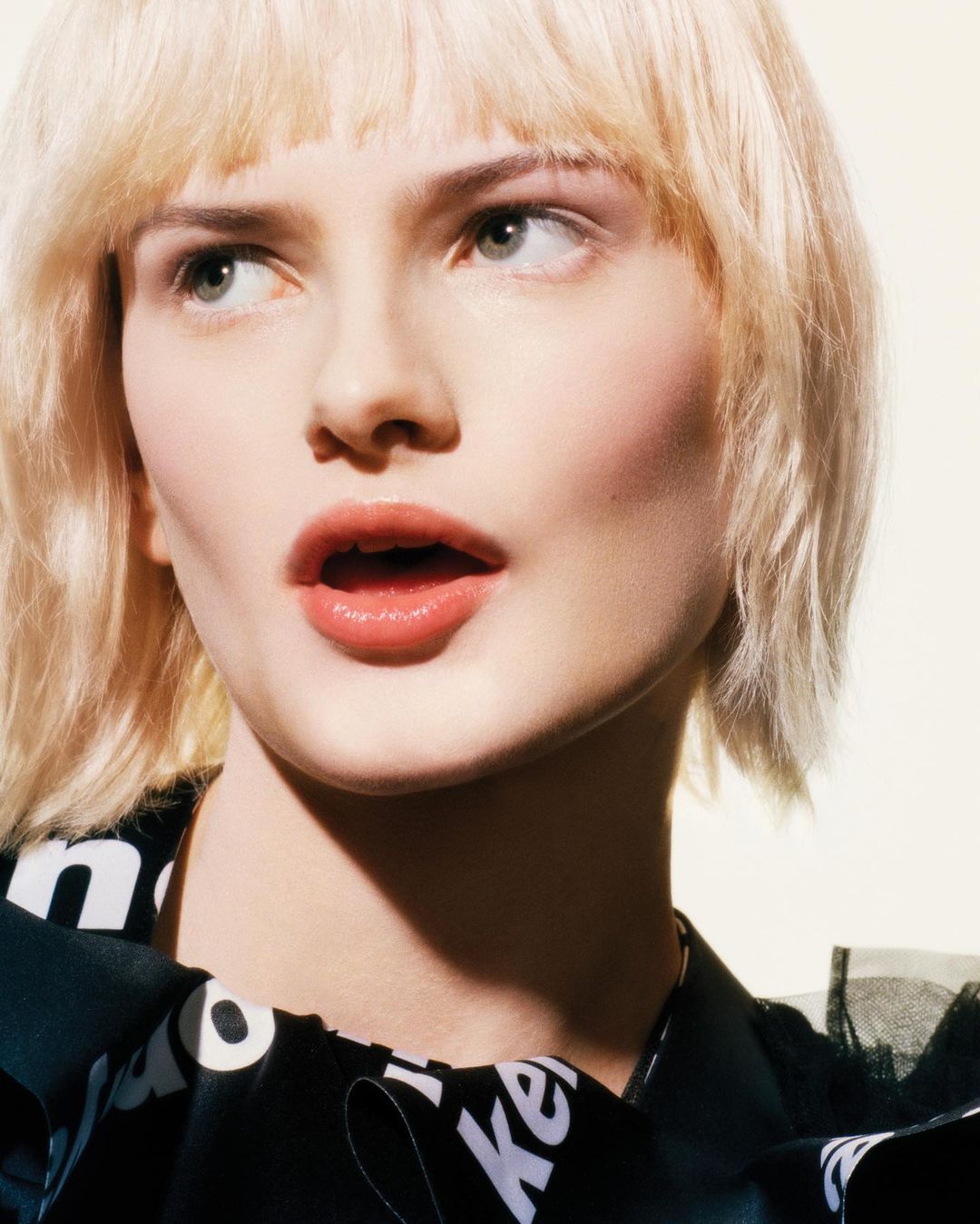 Close-up portrait of a woman with blonde hair wearing a black and white patterned top, looking to the side in a photo studio setting.