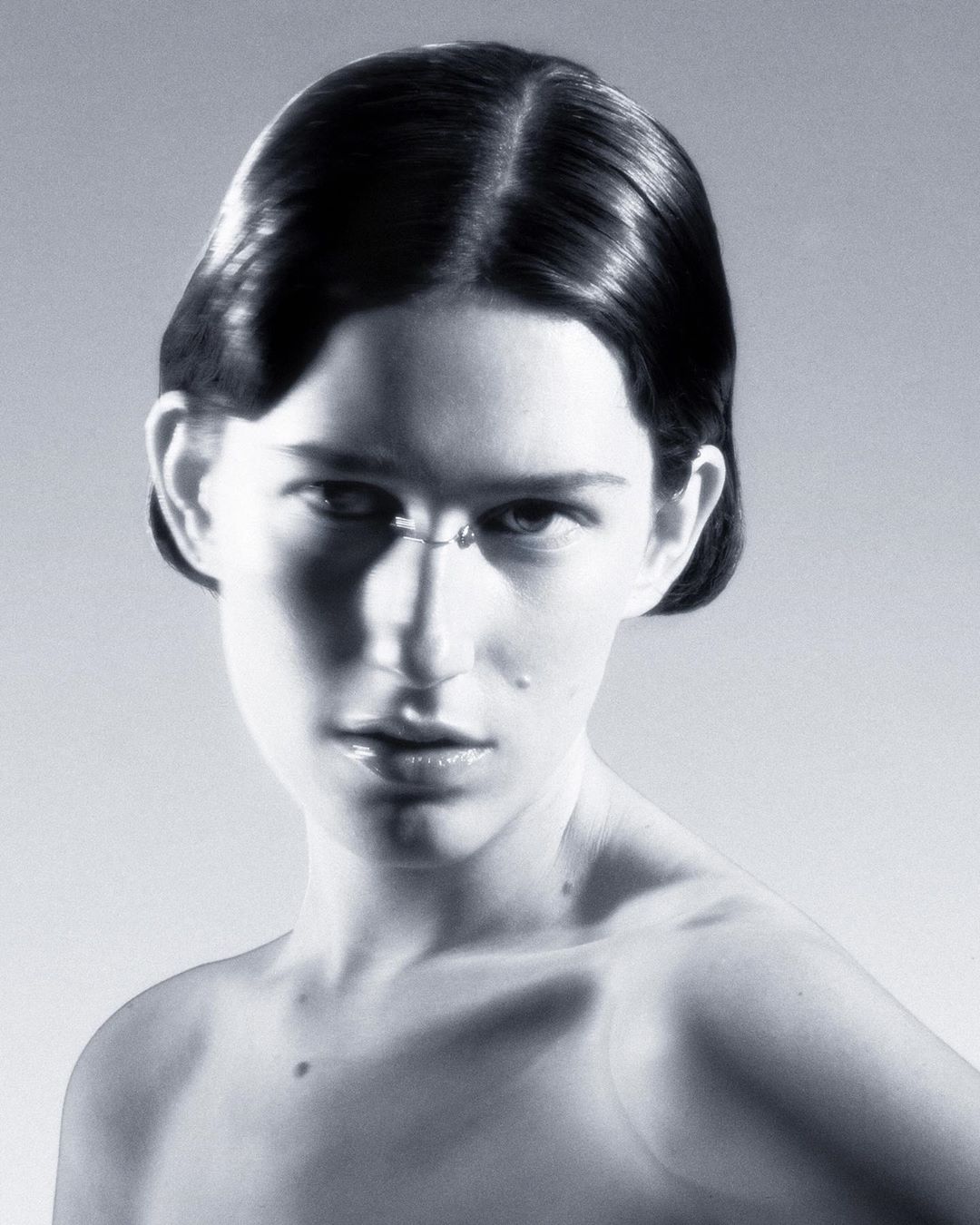 Close-up portrait of an adult woman with short dark hair in a neutral studio setting with soft lighting, showcasing beauty and simple styling.