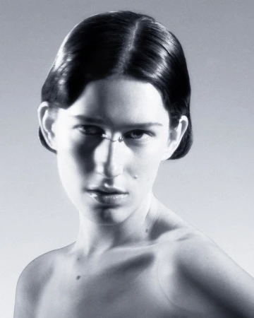 Close-up portrait of an adult woman with short dark hair in a neutral studio setting with soft lighting, showcasing beauty and simple styling.