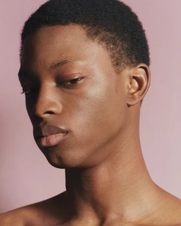 Close-up portrait of a young Black man with short dark hair against a solid pale pink background by Arnaud Lajeunie