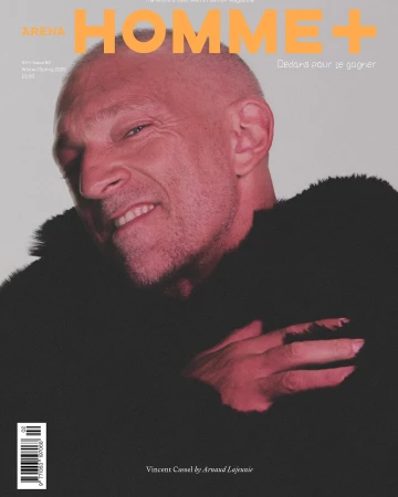 Arena Homme+ magazine cover featuring a close-up of a smiling adult male with short hair and a dark textured jacket against a light background.