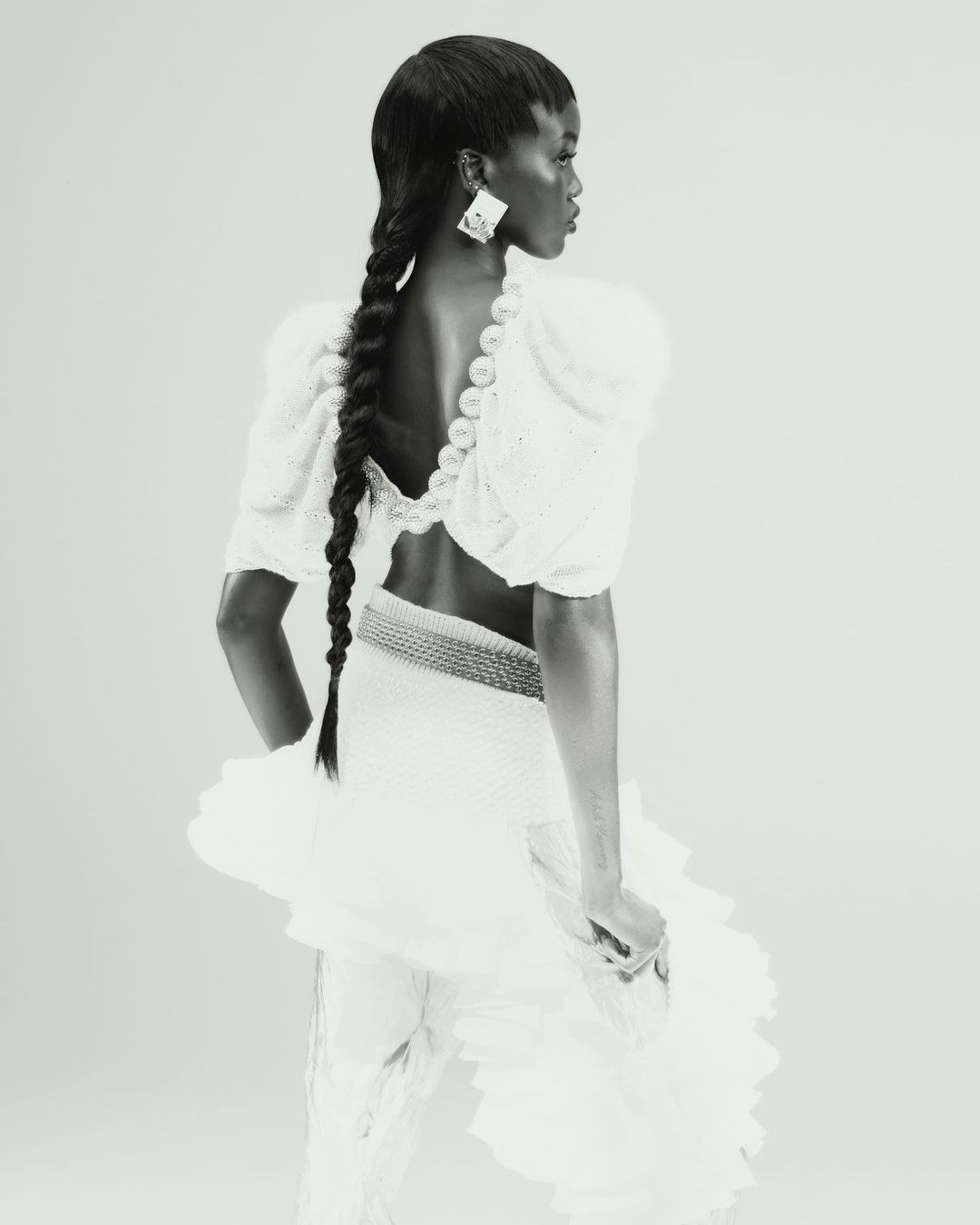 Monochrome portrait of a Black woman with long braids, wearing a white dress with puffed sleeves and large geometric earrings.