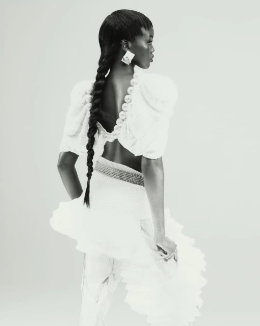 Monochrome portrait of a Black woman with long braids, wearing a white dress with puffed sleeves and large geometric earrings.