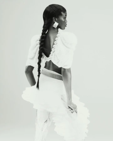 Monochrome portrait of a Black woman with long braids, wearing a white dress with puffed sleeves and large geometric earrings.